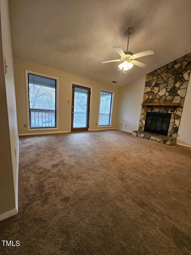 unfurnished living room featuring a textured ceiling, vaulted ceiling, ceiling fan, carpet floors, and a stone fireplace