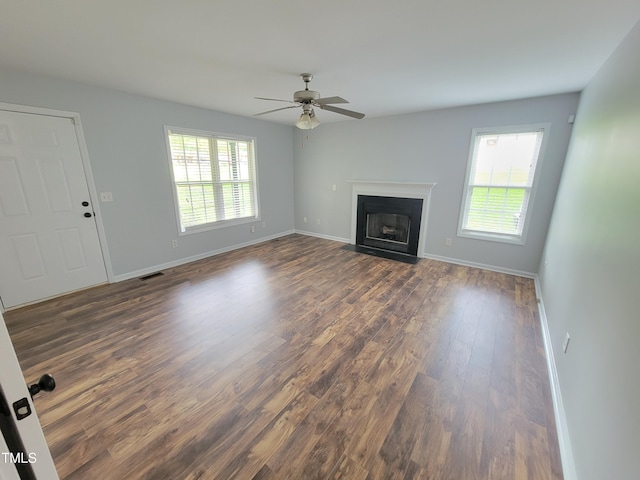 unfurnished living room featuring ceiling fan, plenty of natural light, and dark wood-type flooring