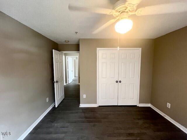 unfurnished bedroom featuring ceiling fan, a closet, and dark wood-type flooring