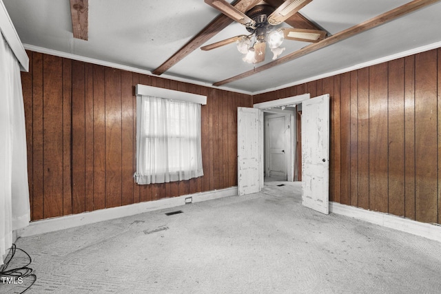 unfurnished bedroom featuring wood walls, ceiling fan, ornamental molding, beamed ceiling, and light colored carpet