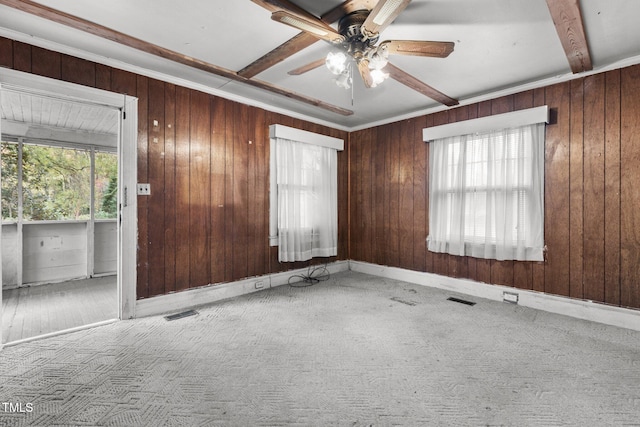 carpeted spare room featuring beam ceiling, plenty of natural light, wooden walls, and ceiling fan