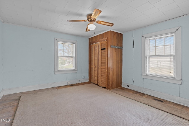 unfurnished bedroom featuring multiple windows, ceiling fan, a closet, and wood walls