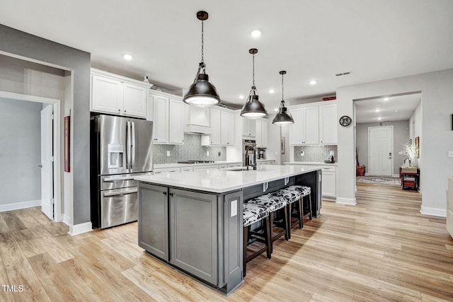 kitchen with white cabinets, stainless steel fridge, a kitchen breakfast bar, and an island with sink