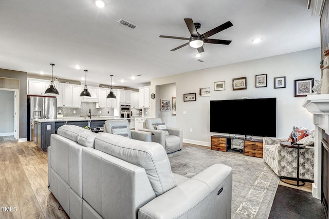 living room featuring a fireplace, light hardwood / wood-style floors, ceiling fan, and sink