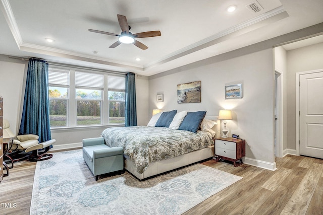 bedroom with ornamental molding, a tray ceiling, wood finished floors, and baseboards