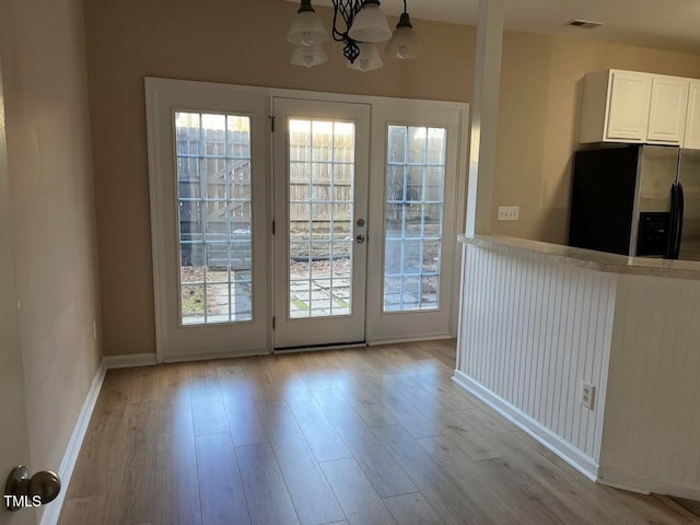 interior space with an inviting chandelier, refrigerator with ice dispenser, decorative light fixtures, light hardwood / wood-style floors, and white cabinetry