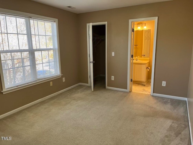 unfurnished bedroom with ensuite bath, light colored carpet, sink, a spacious closet, and a closet