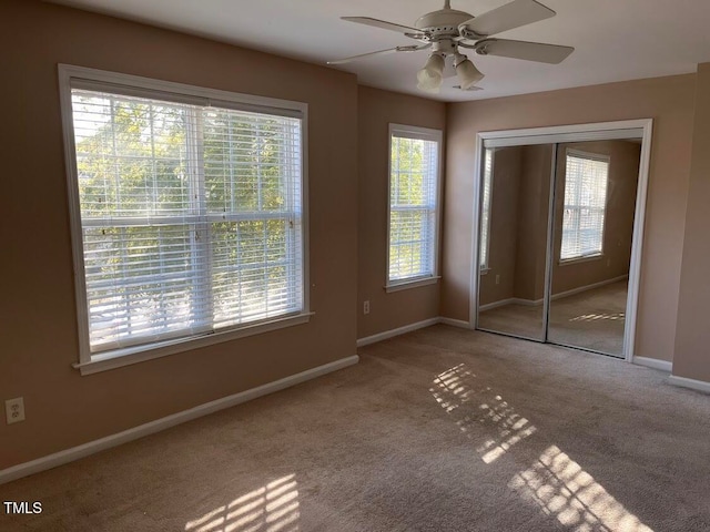 unfurnished bedroom featuring multiple windows, ceiling fan, a closet, and carpet