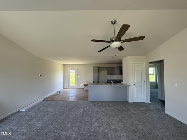 unfurnished living room featuring a ceiling fan, dark colored carpet, a sink, lofted ceiling, and baseboards