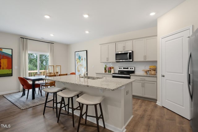kitchen featuring stainless steel appliances, a sink, a kitchen island with sink, backsplash, and a breakfast bar area