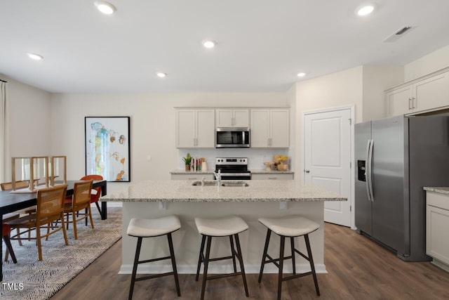 kitchen with stainless steel appliances, dark wood-style floors, an island with sink, a sink, and a kitchen bar