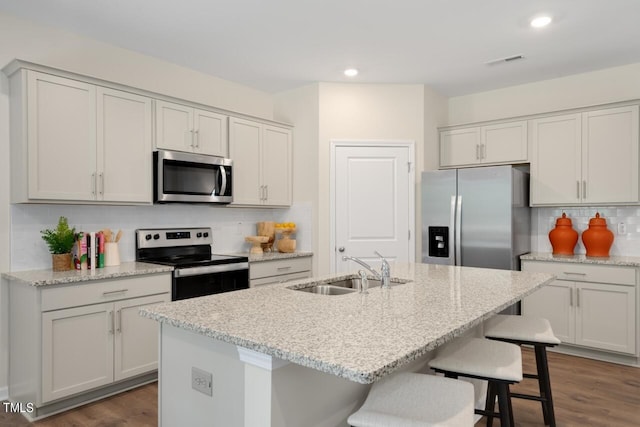 kitchen with appliances with stainless steel finishes, a sink, tasteful backsplash, a kitchen bar, and dark wood-style flooring