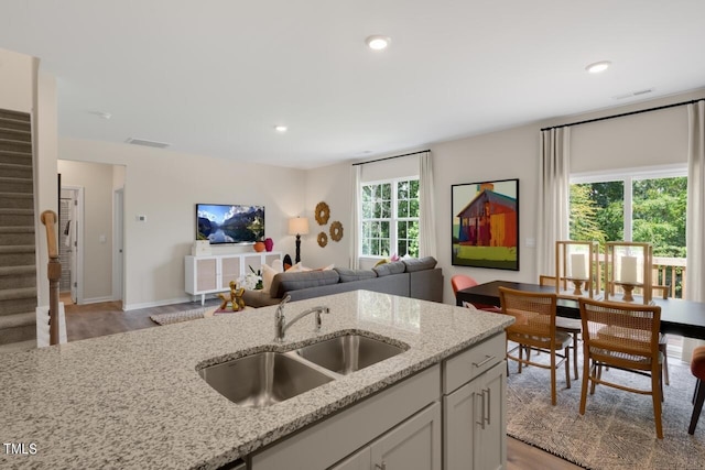 kitchen with a sink, light wood-style floors, light stone counters, open floor plan, and white cabinets