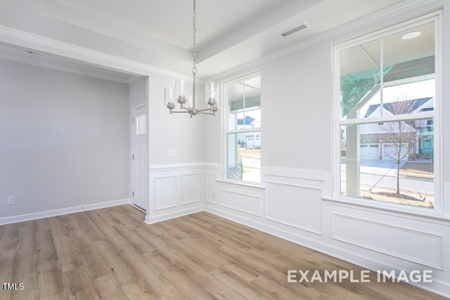 unfurnished dining area with a raised ceiling, a chandelier, and light hardwood / wood-style floors