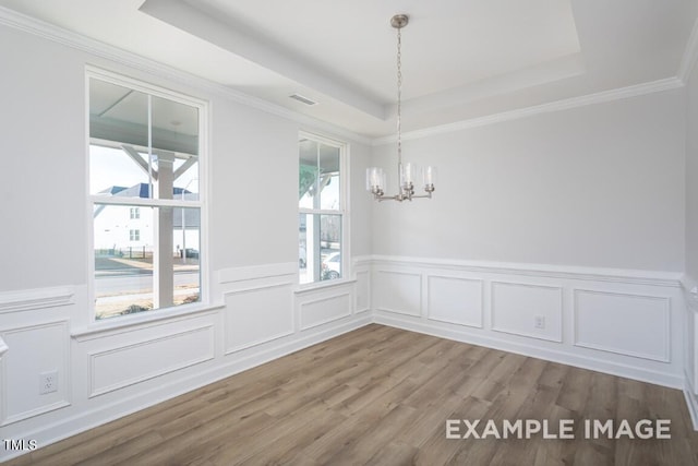 unfurnished dining area with a raised ceiling, crown molding, hardwood / wood-style floors, and a chandelier