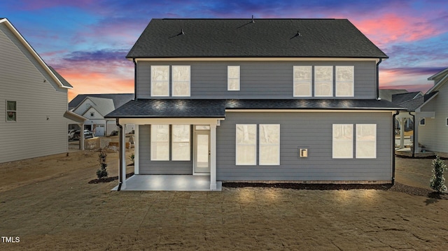 back of property at dusk featuring a shingled roof and a patio