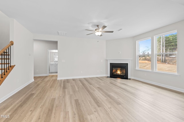 unfurnished living room with light wood finished floors, visible vents, stairway, a fireplace with flush hearth, and baseboards