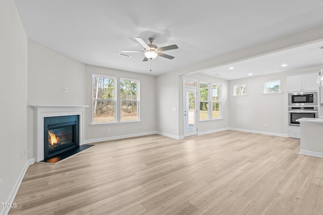 unfurnished living room with light wood-style floors, a glass covered fireplace, ceiling fan, and baseboards