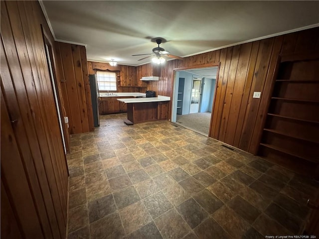 kitchen featuring wood walls, sink, ceiling fan, stainless steel fridge, and kitchen peninsula