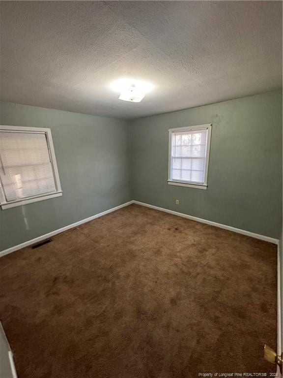 unfurnished room with dark carpet and a textured ceiling