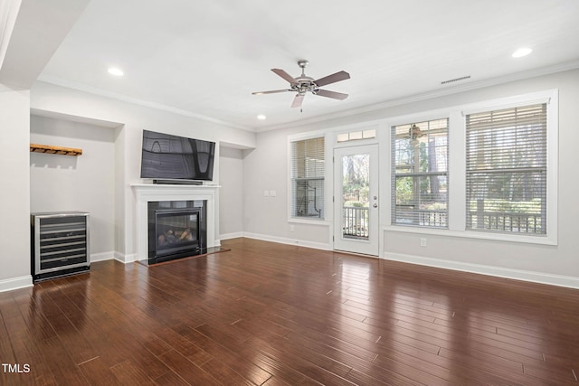 unfurnished living room featuring ceiling fan, beverage cooler, dark hardwood / wood-style flooring, and crown molding