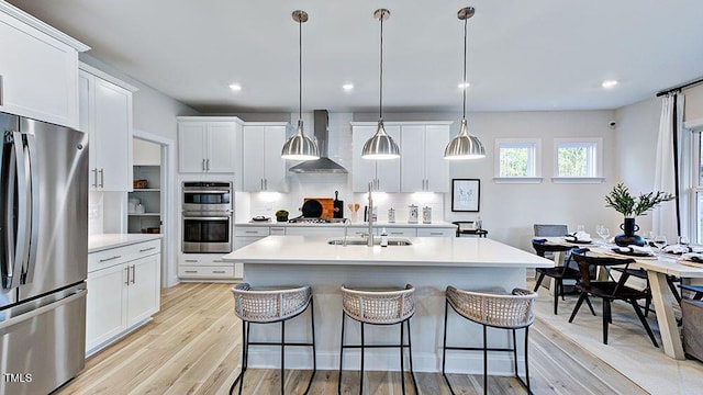 kitchen with white cabinetry, wall chimney range hood, hanging light fixtures, and appliances with stainless steel finishes