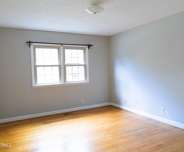 empty room with a textured ceiling and light hardwood / wood-style floors