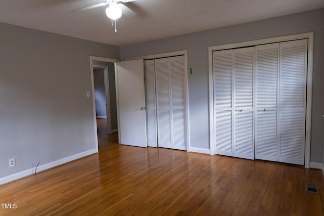 unfurnished bedroom featuring hardwood / wood-style floors, ceiling fan, and multiple closets