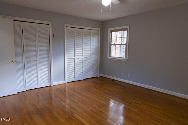 unfurnished bedroom featuring hardwood / wood-style flooring, ceiling fan, and two closets