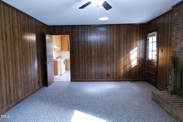 unfurnished living room featuring ceiling fan, light colored carpet, and wooden walls