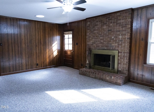 unfurnished living room with carpet, a brick fireplace, ceiling fan, and wood walls