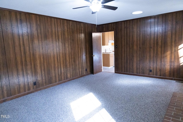 carpeted spare room with ceiling fan and wood walls