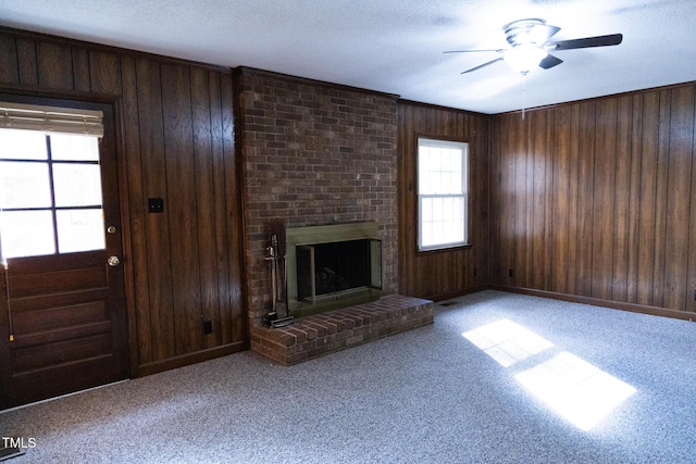 unfurnished living room featuring ceiling fan, light colored carpet, a textured ceiling, wooden walls, and a fireplace