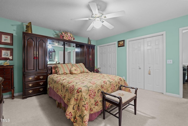 carpeted bedroom featuring a textured ceiling, two closets, and ceiling fan