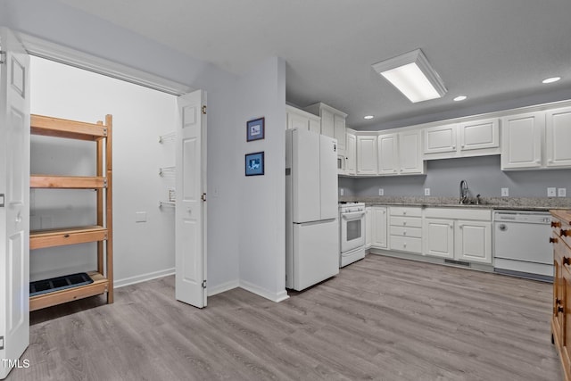 kitchen with light stone countertops, white appliances, sink, white cabinets, and light hardwood / wood-style floors