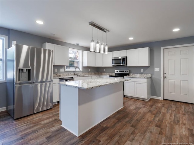 kitchen with hanging light fixtures, white cabinets, dark hardwood / wood-style flooring, a kitchen island, and appliances with stainless steel finishes