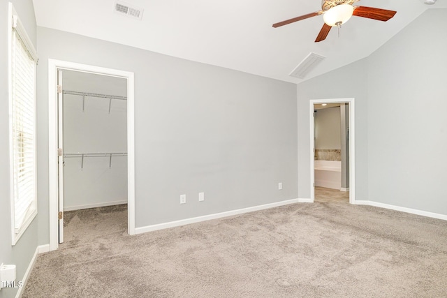 unfurnished bedroom with carpet, vaulted ceiling, visible vents, a walk in closet, and baseboards