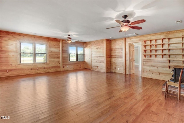 unfurnished living room with hardwood / wood-style floors, a wood stove, ceiling fan, and wooden walls