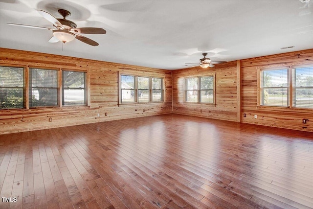 unfurnished room featuring hardwood / wood-style floors, ceiling fan, and wooden walls