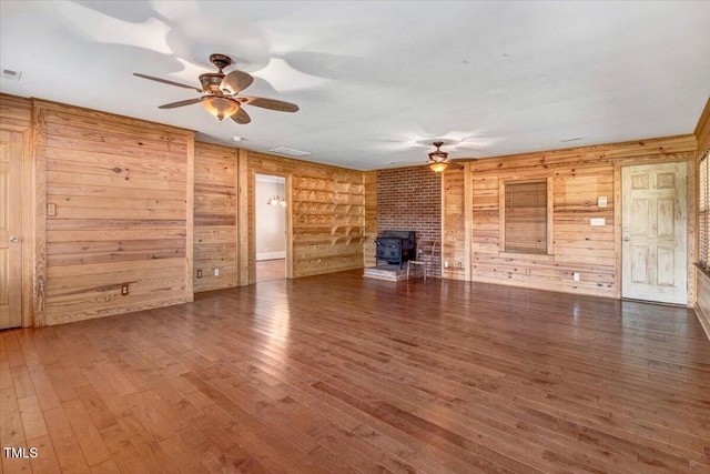 unfurnished living room featuring dark hardwood / wood-style floors, a wood stove, and wooden walls