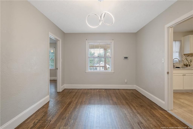 unfurnished dining area featuring sink, dark hardwood / wood-style floors, and a notable chandelier