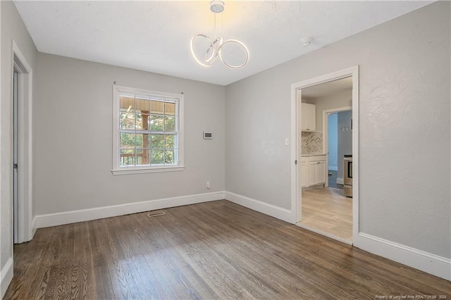 spare room featuring a chandelier and wood-type flooring