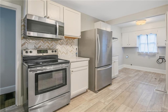 kitchen with backsplash, white cabinets, light wood-type flooring, and appliances with stainless steel finishes