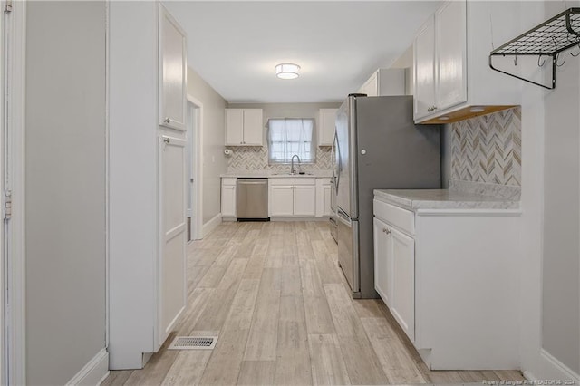 kitchen featuring sink, light hardwood / wood-style flooring, decorative backsplash, white cabinetry, and stainless steel appliances