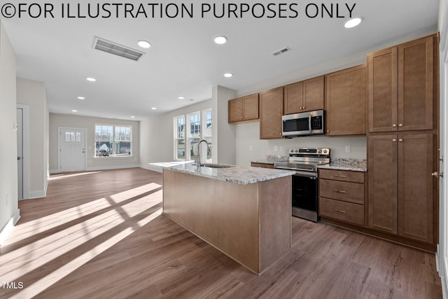 kitchen featuring appliances with stainless steel finishes, light wood-type flooring, light stone counters, sink, and a center island with sink