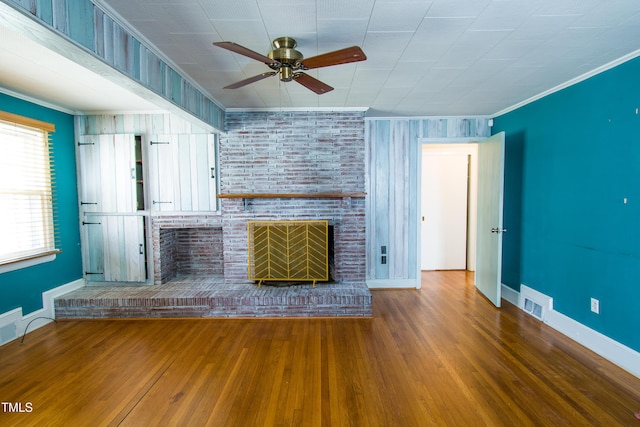 unfurnished living room with ornamental molding, wood finished floors, baseboards, a brick fireplace, and ceiling fan