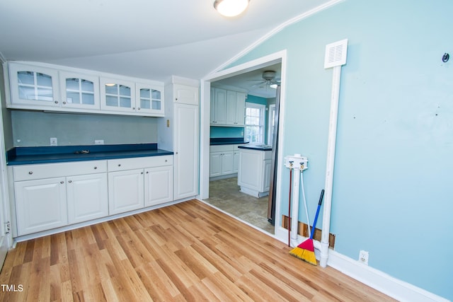 kitchen with visible vents, glass insert cabinets, vaulted ceiling, light wood-style flooring, and white cabinetry