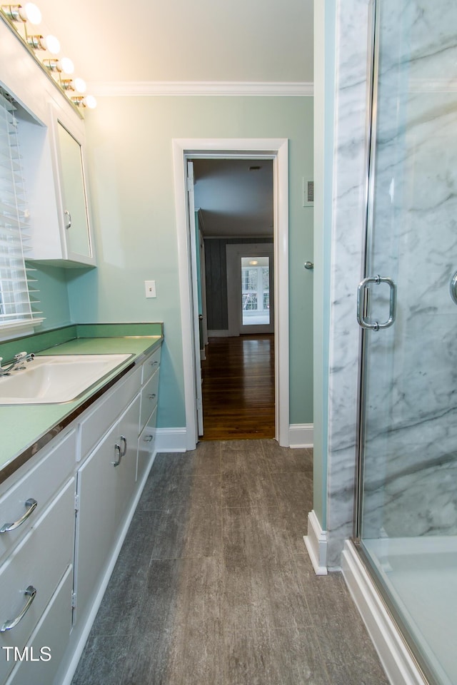 bathroom with wood finished floors, a marble finish shower, crown molding, baseboards, and vanity