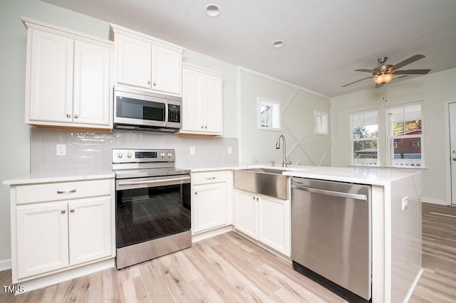 kitchen with white cabinets, kitchen peninsula, stainless steel appliances, and light hardwood / wood-style flooring