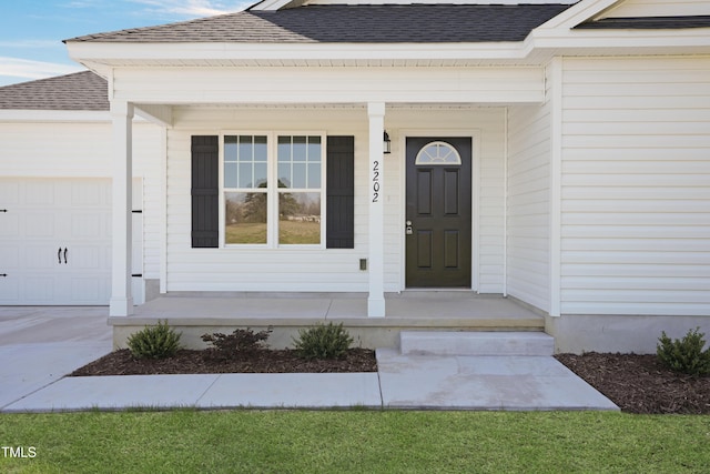 view of exterior entry featuring a porch, an attached garage, roof with shingles, and driveway